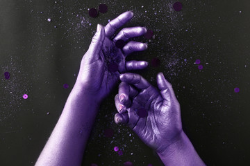 Fototapeta na wymiar Purple female hands with sequins and powder on dark background