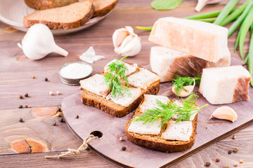 Sandwiches from rye bread, salted bacon and dill on a cutting board on a wooden table