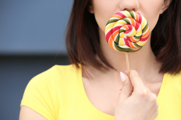 Beautiful young woman with lollipop on grey background, closeup