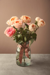 Obraz premium Vase with bouquet of beautiful roses on table against color background