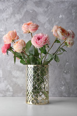 Vase with bouquet of beautiful roses on table against grey textured background