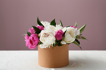 Box with beautiful peony flowers on table against color background