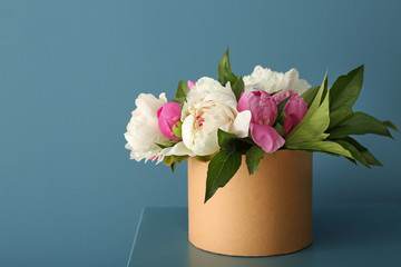 Box with beautiful peony flowers on table against color background