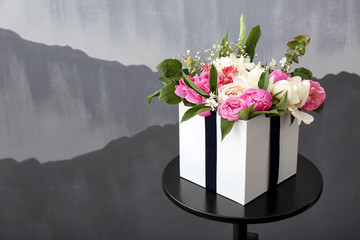 Gift box with beautiful flowers on table against grey background
