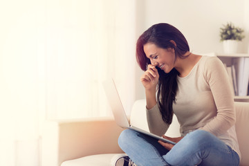 Laghing woman using a laptop sitting on a couch