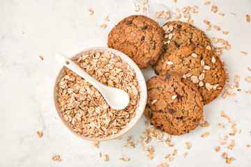 Bowl with oatmeal and delicious cookies on light background