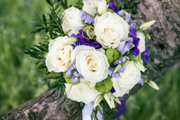 Fototapeta na wymiar White roses with blue and lavender flowers bouquet. Wedding ring macro photography. Beautiful bridal bouquet with white roses and golden rings