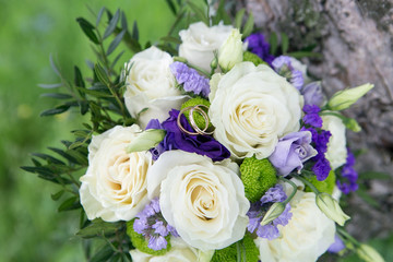 Fototapeta na wymiar White roses with blue and lavender flowers bouquet. Wedding ring macro photography. Beautiful bridal bouquet with white roses and golden rings
