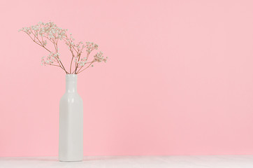 Small white dried flowers in elegant high ceramic vase on soft pastel pink background, copy space. Fashion home decor.