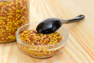 French mustard in small glass bowl with black ceramic spoon