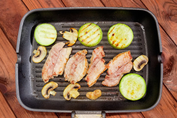 Grill pan with grilled streaky bacon, vegetable marrows and mushrooms