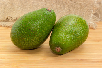 Two whole green avocado fruits on a wooden surface