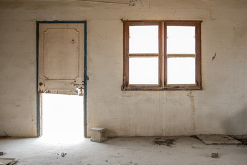 A window and broken door in the wall of a room in an abandoned, derelict building with stained walls.