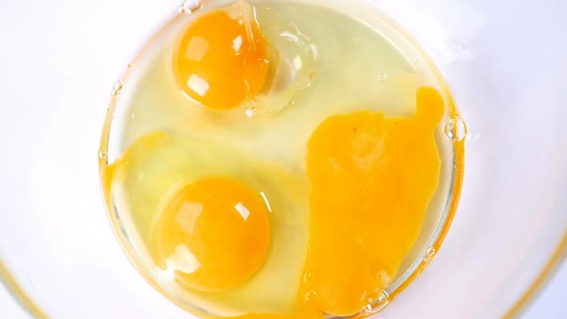 Breaking eggs in a glass bowl. Fresh organic eggs falling into bowl. Preparing ingredients for baking. Slow motion footage.