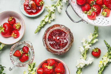Strawberries homemade jam in glass jar with summer flowers and fresh berries on table background, top view. Berries preserve concept