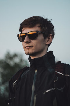 young man in sunglasses on the background of the cloudy sky watching the sunset, the sky is reflected in the glasses of a tourist outdoor
