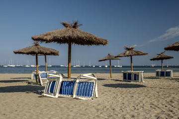 Out of season beach in Spain. The sun is shining, but the sun loungers are chained up to the sun shades and not in use