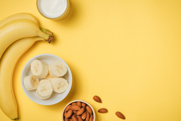 Almond milk in a glass with almond nuts and bananas on a yellow background. Healthy food and drink concept.