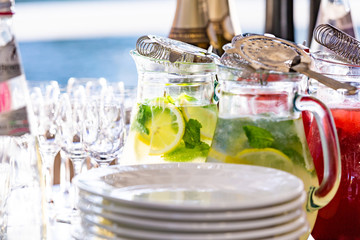two glass jars of home made fresh raspberry lemonade or virgin mojito cocktail with a straw on the table among dishes prepared for serving