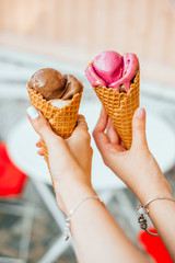 Chocolate and strawberry ice cream in waffle cups in hands of two girls best friends.