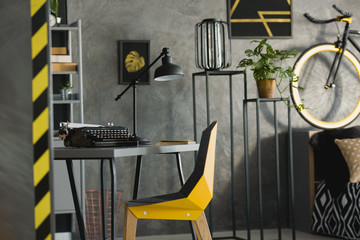 Yellow chair at desk with typewriter and lamp in grey workspace interior. Real photo