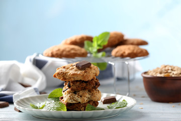 Plate with tasty oatmeal cookies, chocolate and mint leaves on table