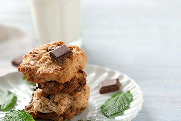Plate with tasty oatmeal cookies, chocolate and mint leaves on table