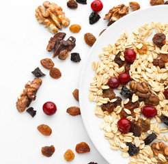Plate with oatmeal, cranberries, raisins and walnuts on white background