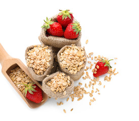 Composition with sacks of raw oatmeal and fresh strawberry on white background
