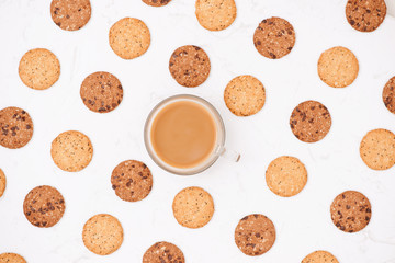 Cup of coffee among pattern of various shortbread and oat cookies with cereals and raisin on black wooden background. Top view, flat lay.