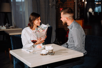 Happy romantic couple in cafe. Young man is presenting flowers to his beloved.