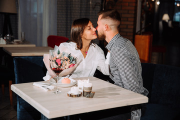 Happy romantic couple in cafe. Young man is presenting flowers to his beloved.