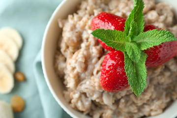 Bowl with tasty oatmeal and strawberry on table, closeup