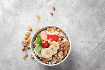 Bowl with tasty oatmeal, sliced banana and strawberry on grey textured background