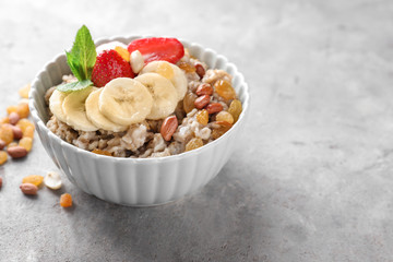 Bowl with tasty oatmeal, sliced banana and strawberry on grey textured background