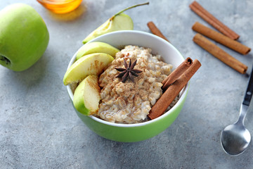 Bowl with tasty oatmeal, sliced apple and spices on grey textured background