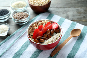 Bowl with tasty oatmeal, sliced berries and nuts on table