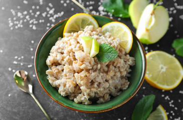 Bowl with tasty oatmeal, fresh apple and sliced lemon on grey background