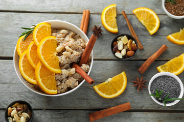 Bowl with tasty oatmeal, sliced orange and cinnamon sticks on wooden table