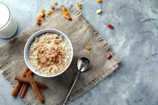 Bowl with tasty oatmeal and cinnamon on grey textured background