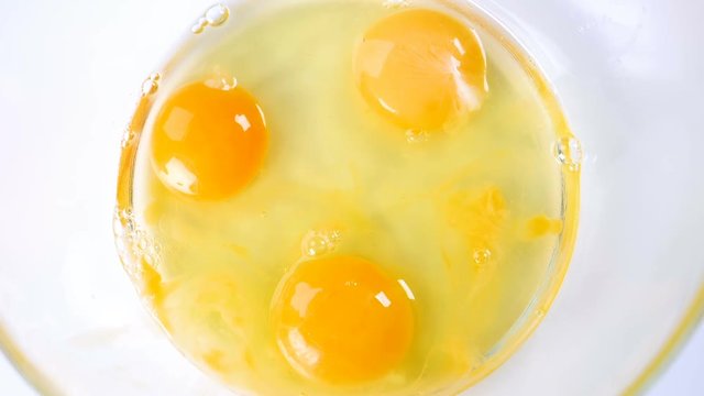 Breaking eggs in a glass bowl. Fresh organic eggs falling into bowl. Preparing ingredients for baking. Slow motion footage.
