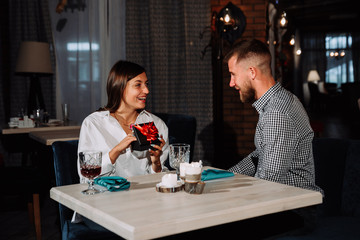 Surprised happy woman sitting by the table on date in cafe and gets the gift.