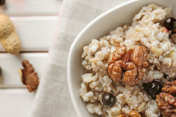 Bowl with tasty oatmeal, berries and nuts on white table