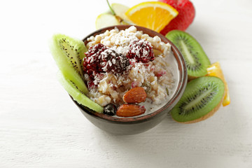 Bowl with tasty oatmeal, berries and fruits on light background