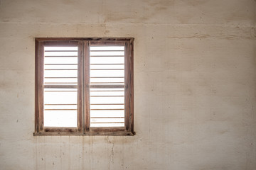 A glassless, barred window in the wall of a room in an abandoned, derelict building with stained walls.