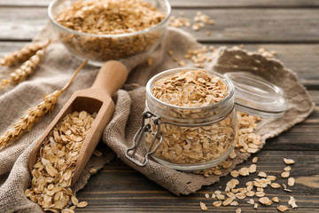 Glass jar and scoop with raw oatmeal on wooden background
