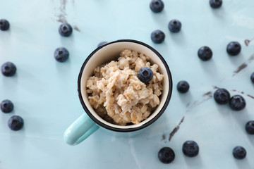 Cup with tasty oatmeal and blueberries on color background
