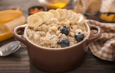 Tureen with tasty oatmeal, sliced banana and fresh berries on wooden table