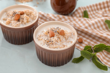 Bowls with tasty oatmeal, milk and nuts on color background