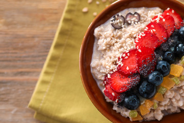 Bowl with tasty oatmeal, fresh berries and candied fruits on table